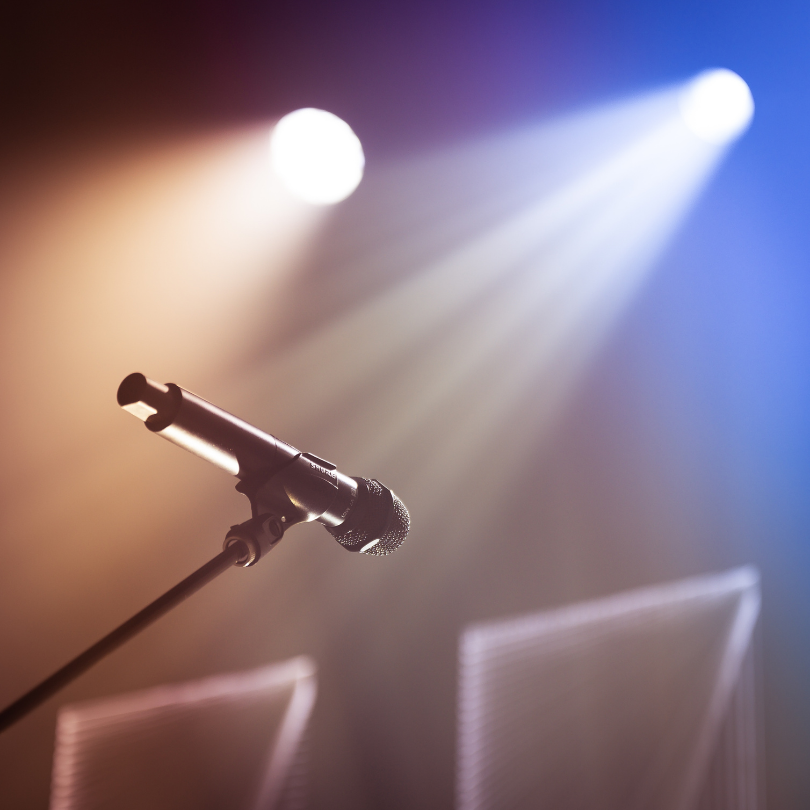 Bühnenmikrofon im Scheinwerferlicht vor unscharfem Hintergrund – bereit für eine Performance oder Ansprache.
