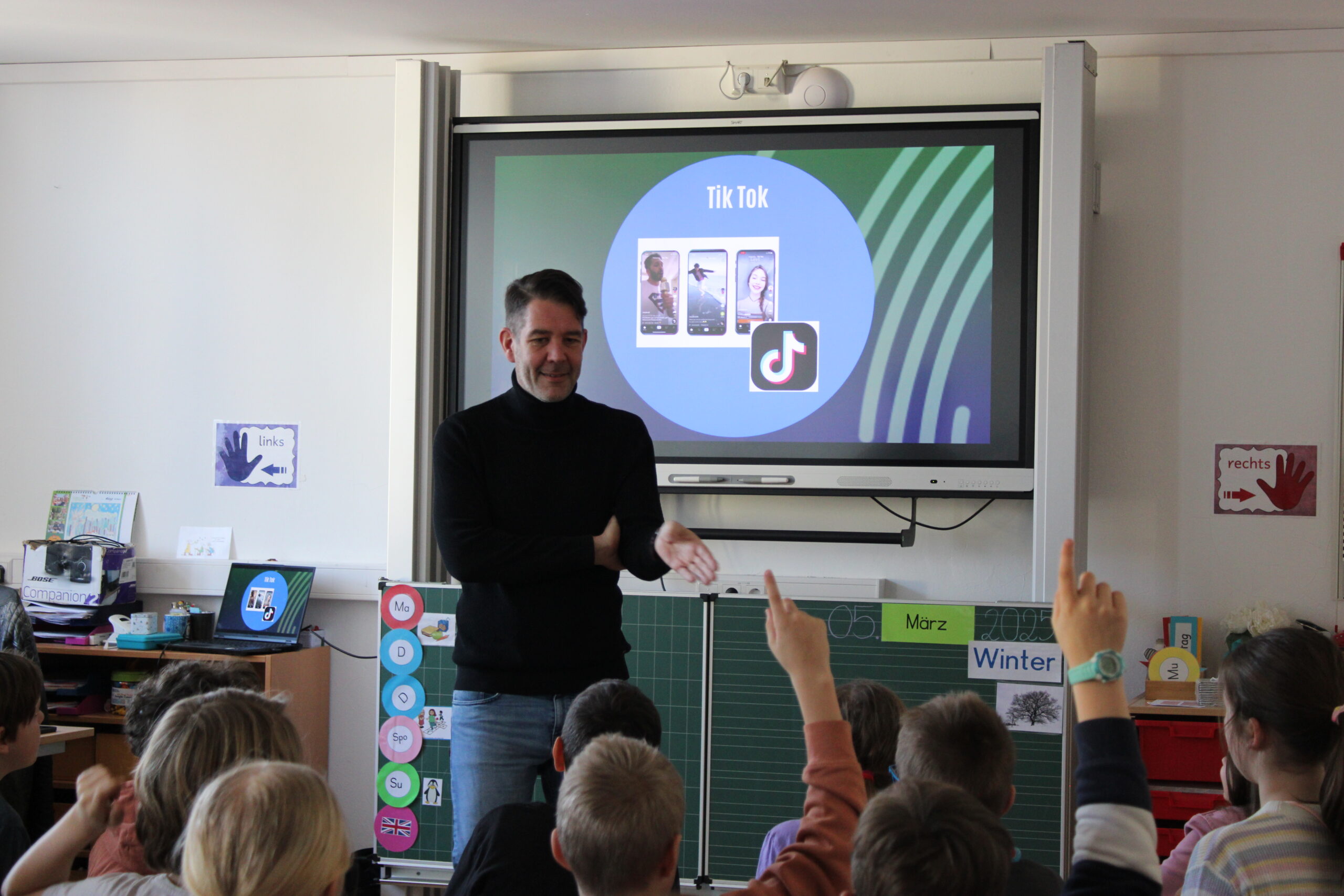 Mann spricht in einem Klassenzimmer mit Grundschulkindern über TikTok im Rahmen eines Medienkompetenz-Workshops.